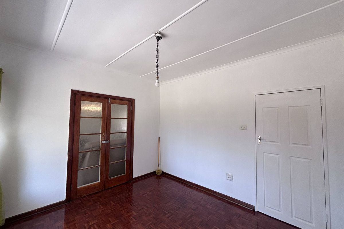 An empty living room featuring polished parquet flooring, classic wooden french doors, and a simple coved ceiling, offering a clean canvas for interior design.