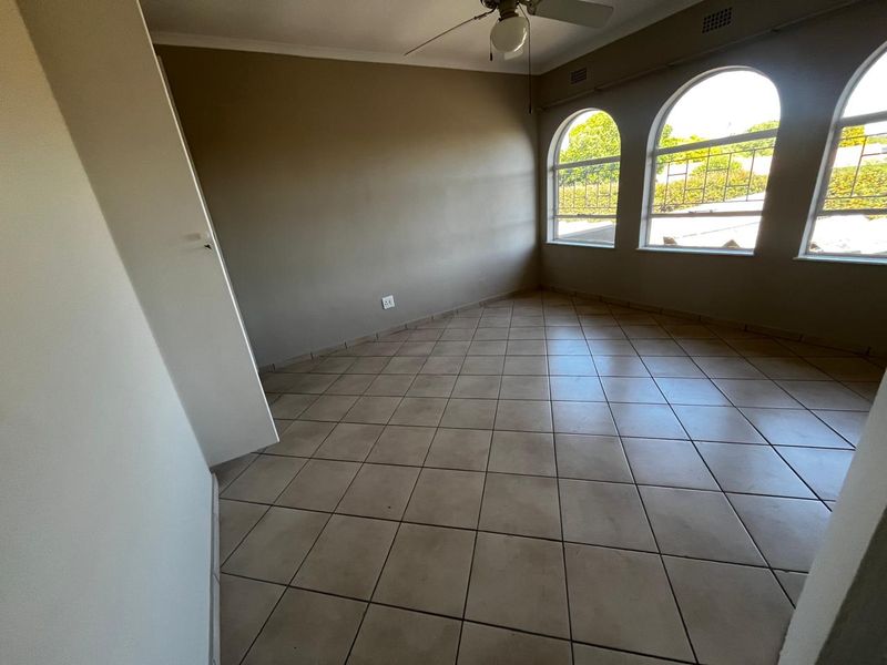 An empty bedroom featuring tiled flooring, a ceiling fan, and distinctive arched windows that provide natural light.