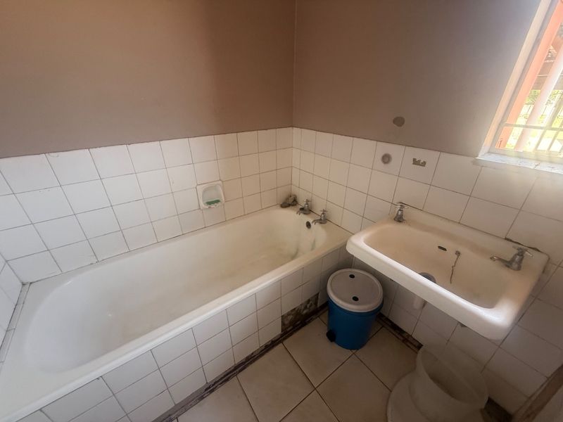 A dated bathroom featuring a built-in bathtub and wall-mounted basin with ceramic tiling, requiring renovation to update the finishes and fixtures.