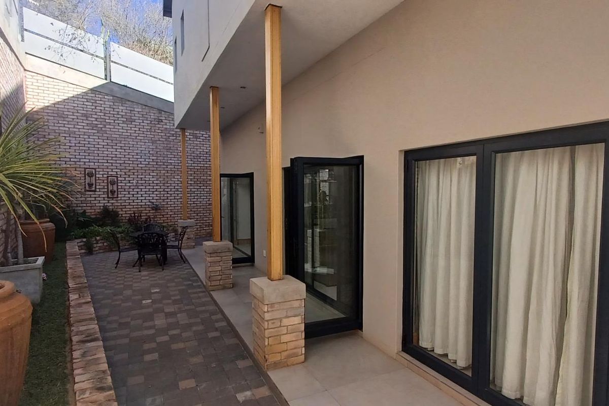 A private rear patio area featuring paved flooring, brick boundary walls, and modern black-framed glass sliding doors leading into the townhouse.