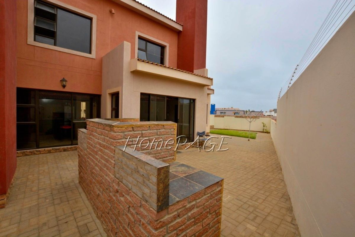 Rear exterior view of the townhouse featuring a paved patio area, built-in brick braai, and a small private garden space.