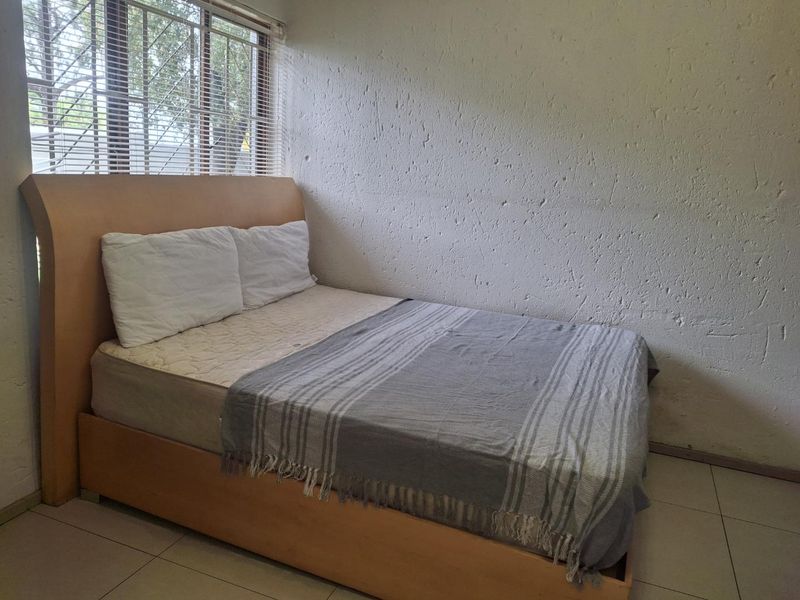 A bedroom featuring tiled flooring, textured walls, and a window fitted with security bars and venetian blinds.