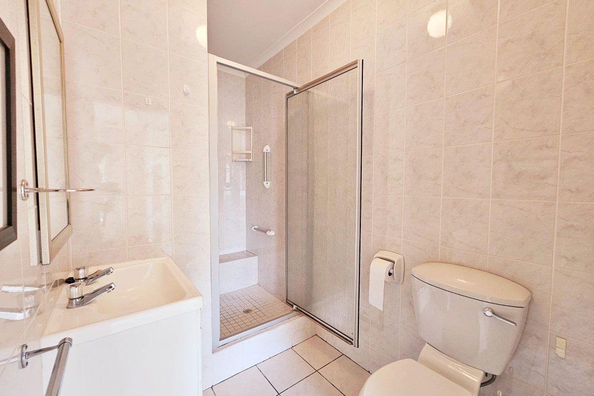 A functional bathroom featuring a shower enclosure, vanity basin, and toilet with neutral wall and floor tiling.