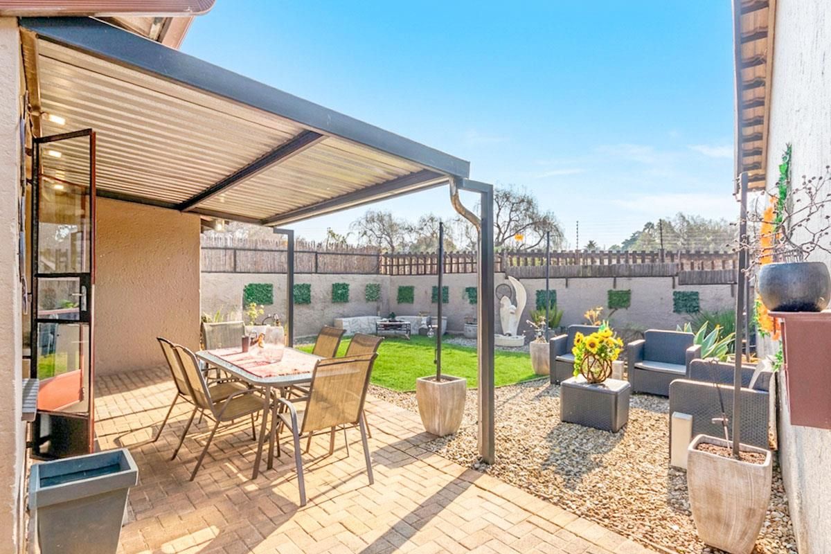 A private rear garden featuring a paved patio area with a covered pergola, lawn space, and perimeter boundary walls.