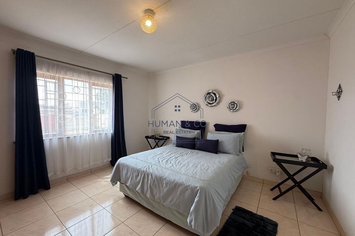 A well-lit bedroom featuring tiled flooring, a large window with security bars, and a central ceiling light fixture.