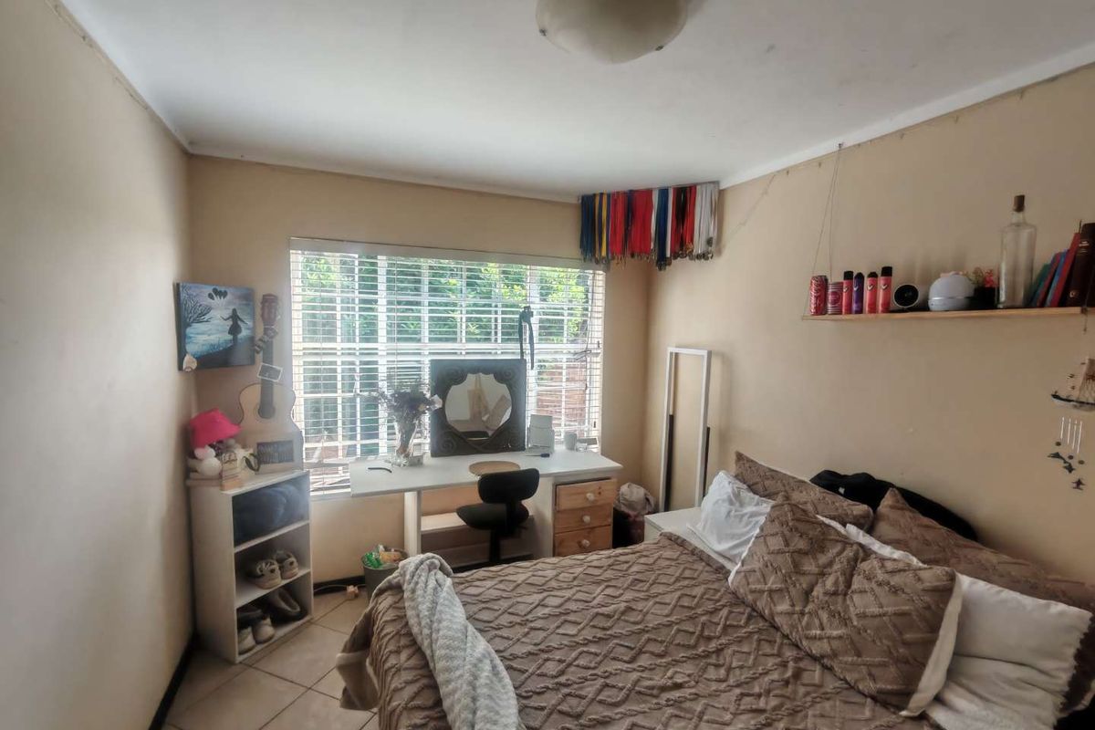 A bedroom featuring tiled flooring, a window with security bars, and a ceiling light fixture. The room requires cosmetic updates to the walls.