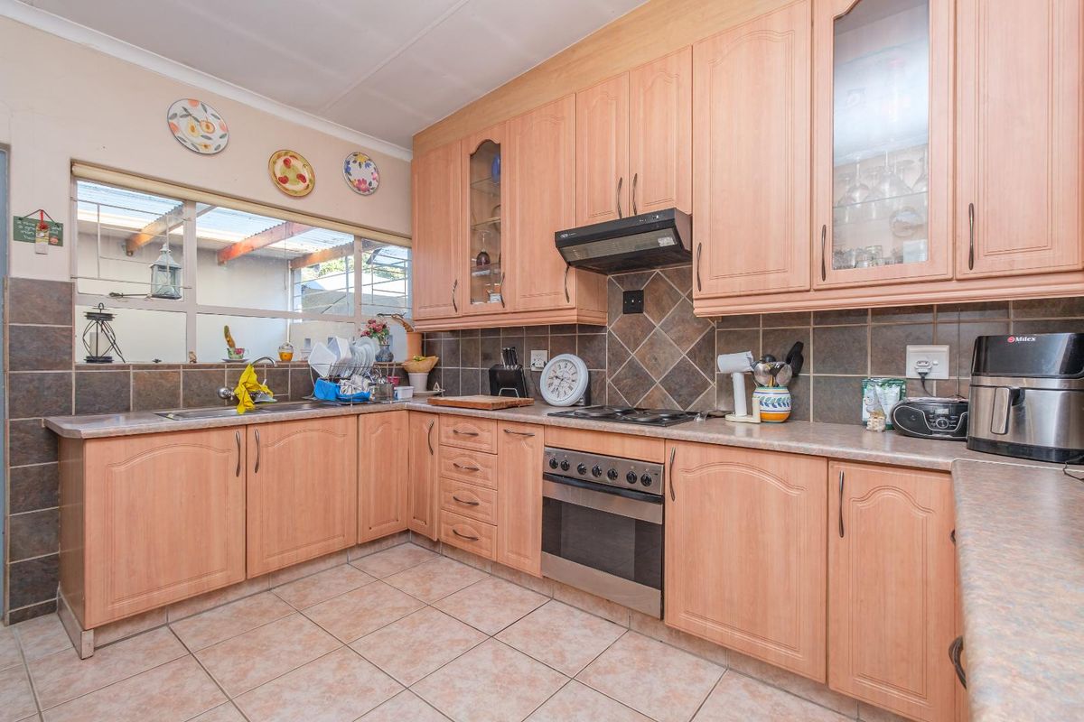A functional kitchen featuring light wood-tone cabinetry, tiled backsplash, built-in oven with hob, and tiled flooring.