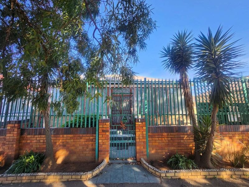 Front elevation of the property featuring a secure brick boundary wall, metal fencing, and a wrought iron pedestrian gate leading to the entrance.