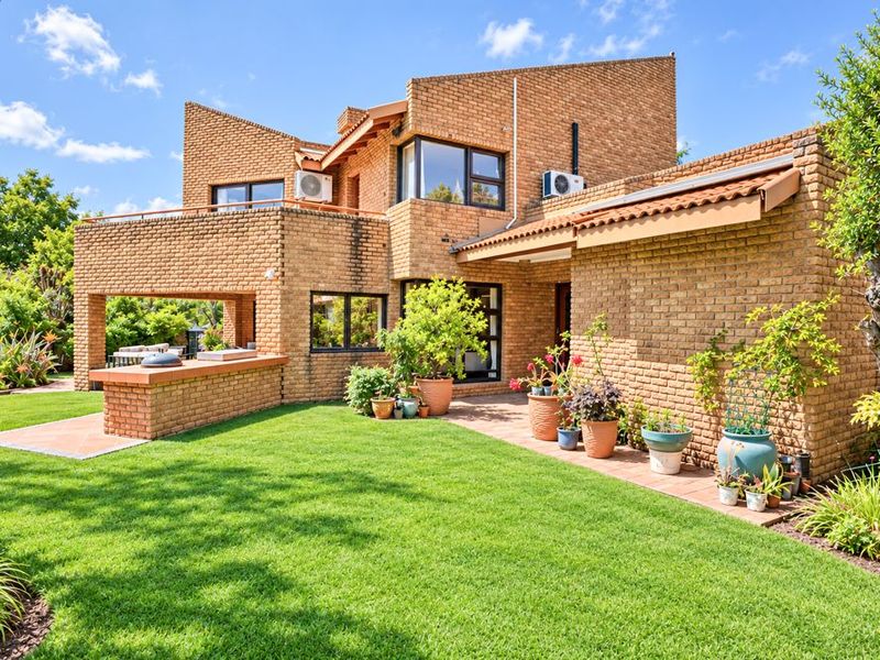 Rear view of a face brick house featuring a landscaped garden, a covered patio area with a built-in brick braai, and established greenery.