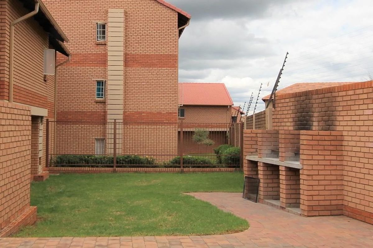 Rear exterior view of the apartment featuring a private garden, paved patio area, and a built-in brick braai facility.