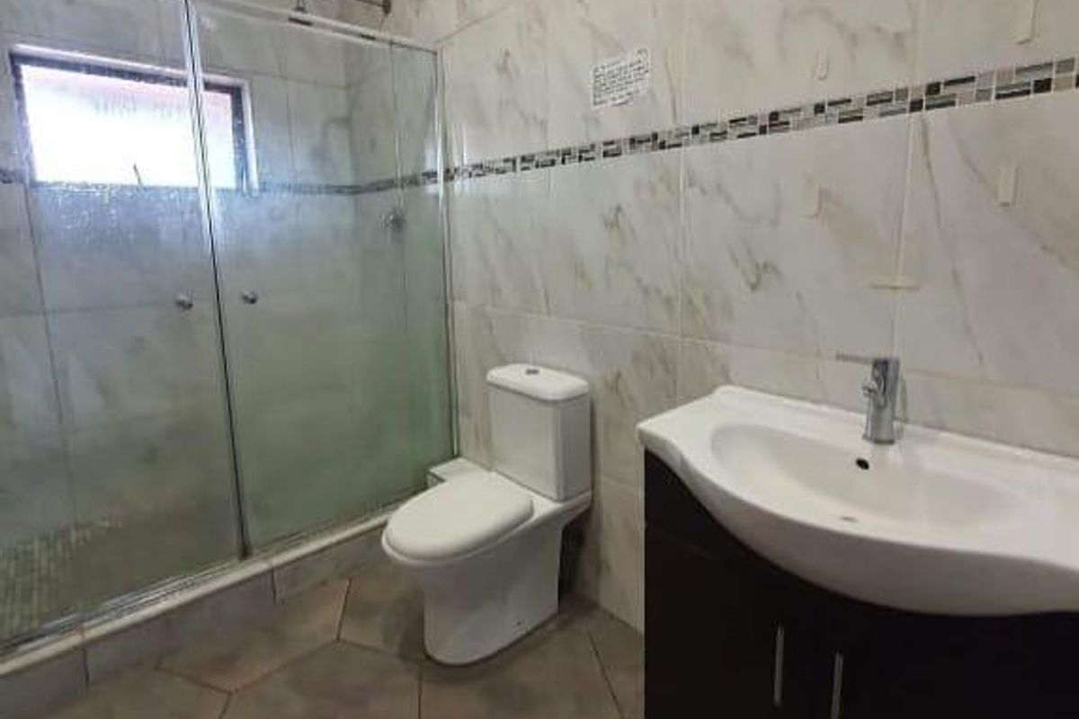 A functional bathroom featuring a glass-enclosed shower, a modern vanity with a basin, and a toilet, finished with marble-look wall tiles.
