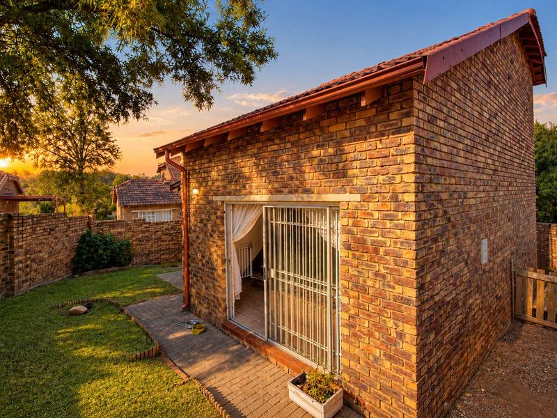 Rear view of a face brick townhouse featuring a paved walkway, secure sliding door access, and a private garden area at sunset.
