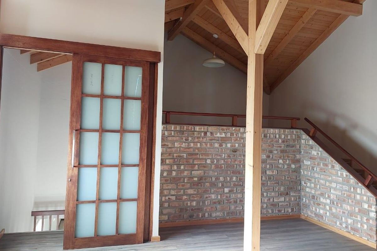 An interior space featuring a vaulted timber ceiling, exposed brick wall, wooden support post, and a sliding glass-paneled door leading to an adjacent room.
