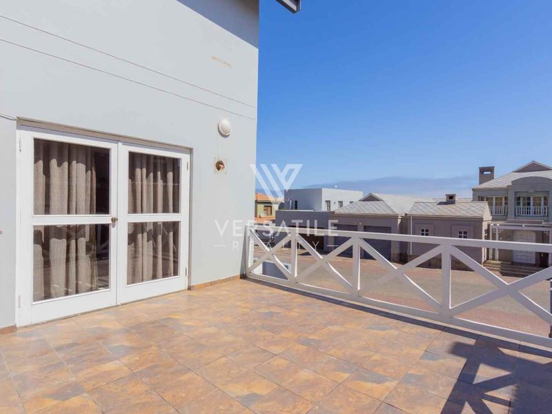 A spacious outdoor balcony featuring tiled flooring and a white wooden balustrade, offering an open area suitable for outdoor seating.