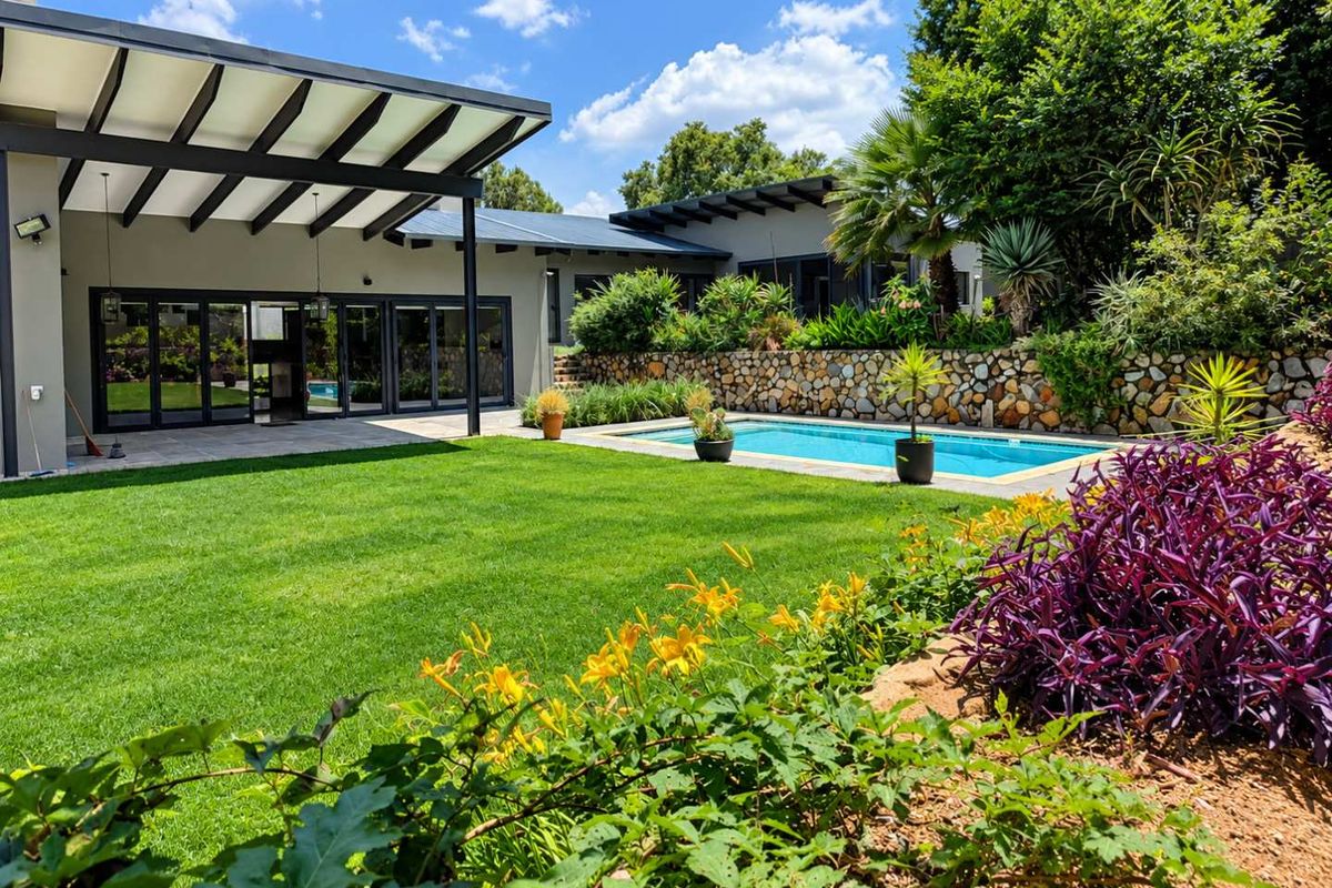 A beautifully landscaped rear garden featuring a swimming pool, stone retaining wall, and a spacious covered patio with modern bi-fold doors.
