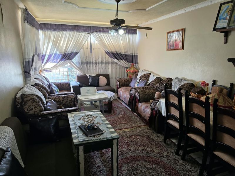 A living room featuring a ceiling fan, decorative molding, and window security bars, showing signs of wear on the walls and ceiling.