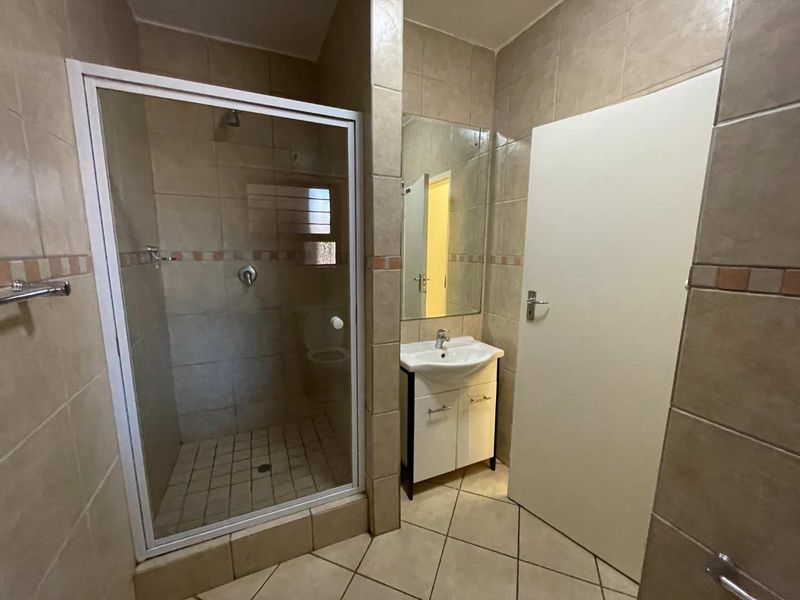 A functional bathroom featuring a tiled shower enclosure, a vanity unit with a washbasin, and neutral wall tiling throughout.