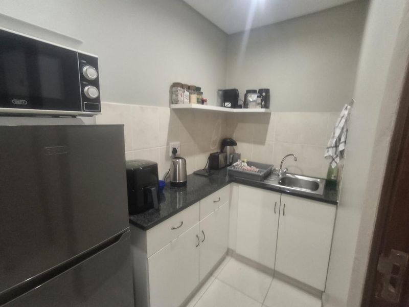Compact scullery area featuring white built-in cabinetry, dark granite countertops, a stainless steel sink, and tiled backsplash.
