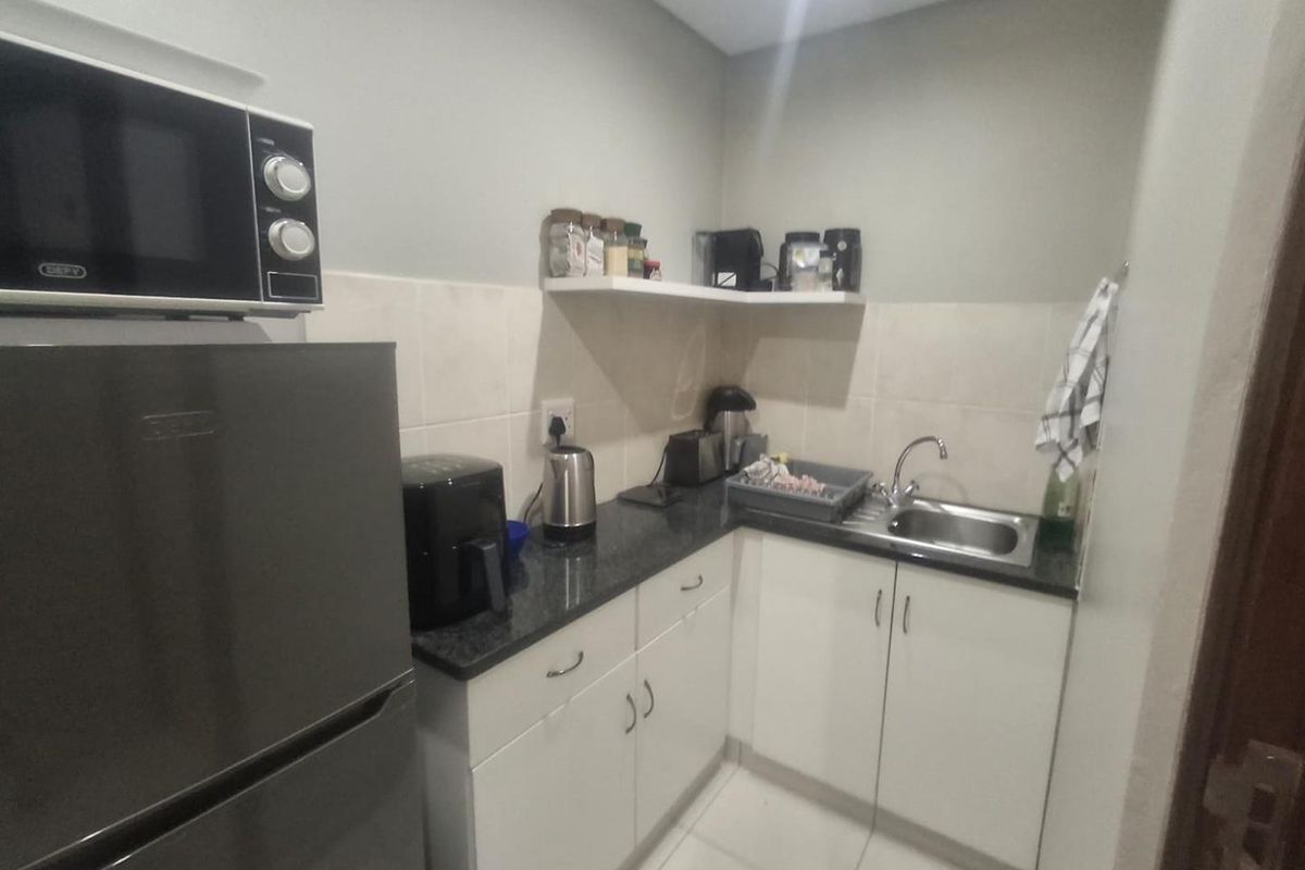 Compact scullery area featuring white built-in cabinetry, dark granite countertops, a stainless steel sink, and tiled backsplash.