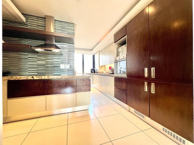 Modern kitchen featuring dark wood and light cabinetry, granite countertops, built-in appliances, and a stylish mosaic tile backsplash with tiled flooring.