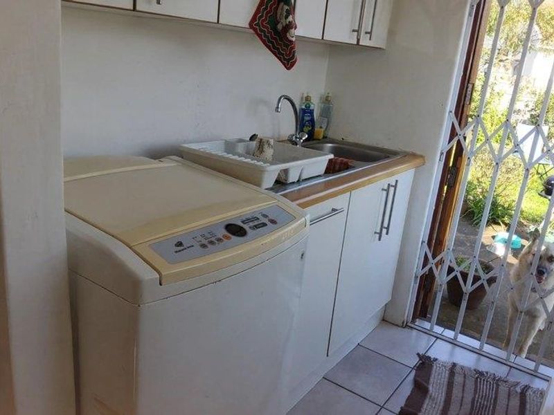 A functional laundry area featuring built-in cabinetry, a stainless steel sink, and tiled flooring, with direct access to the exterior through a security gate.
