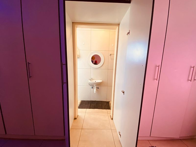 A bathroom featuring tiled walls and flooring, a wall-mounted basin, and flanked by built-in cupboards in the adjacent room.