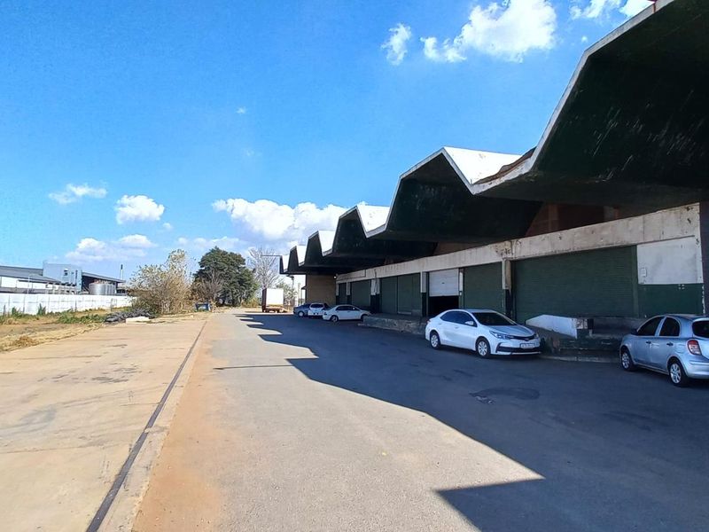 Industrial warehouse exterior featuring a distinctive sawtooth roof design, large loading bays, and expansive concrete yard space for logistics and vehicle access.