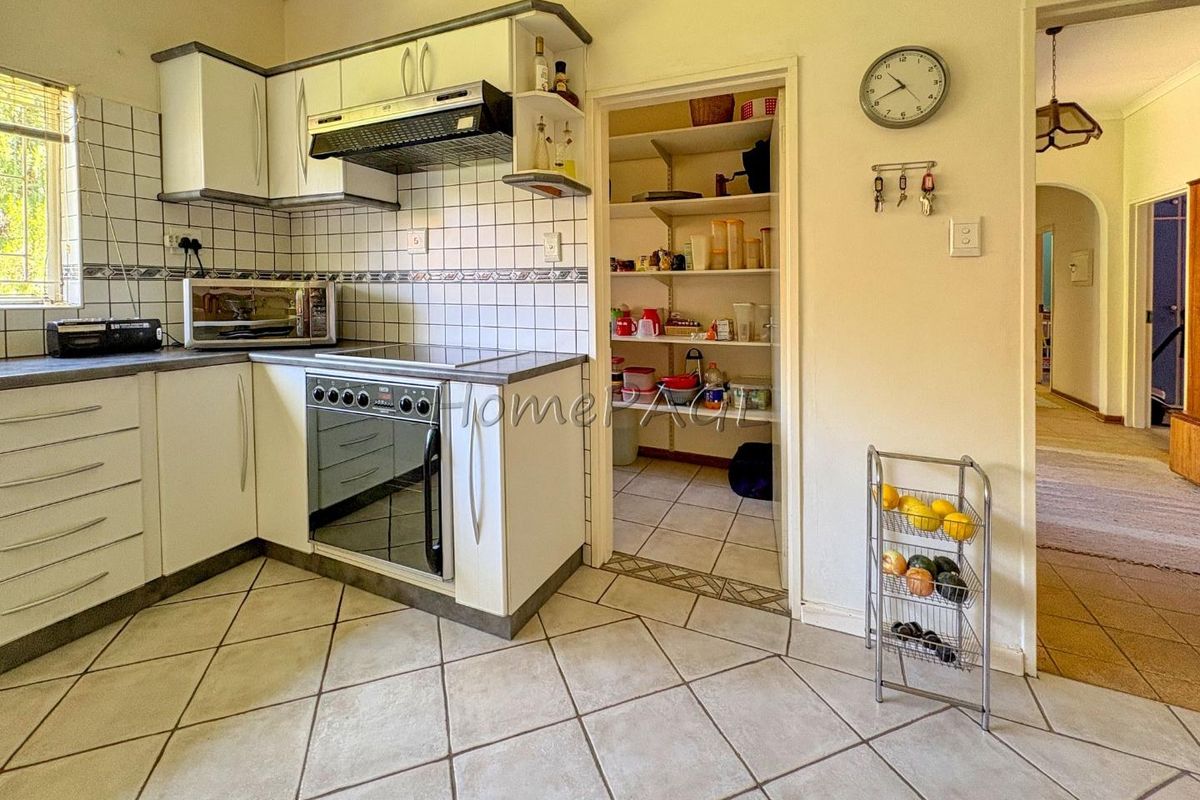 A functional kitchen featuring tiled flooring, built-in cabinetry, a stove with extractor fan, and an adjacent walk-in pantry or scullery area.