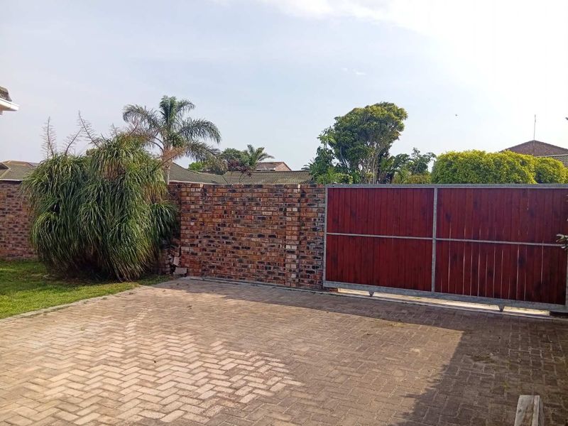 A paved driveway entrance featuring a sliding timber and steel gate with an adjacent brick boundary wall.