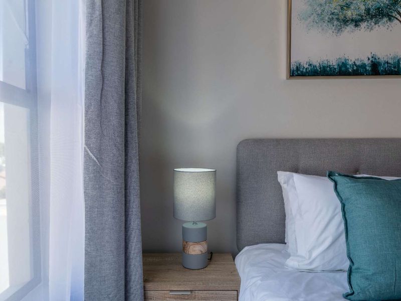 A close-up view of a bedroom corner featuring a neutral wall, window with curtains, and space for a bedside table.