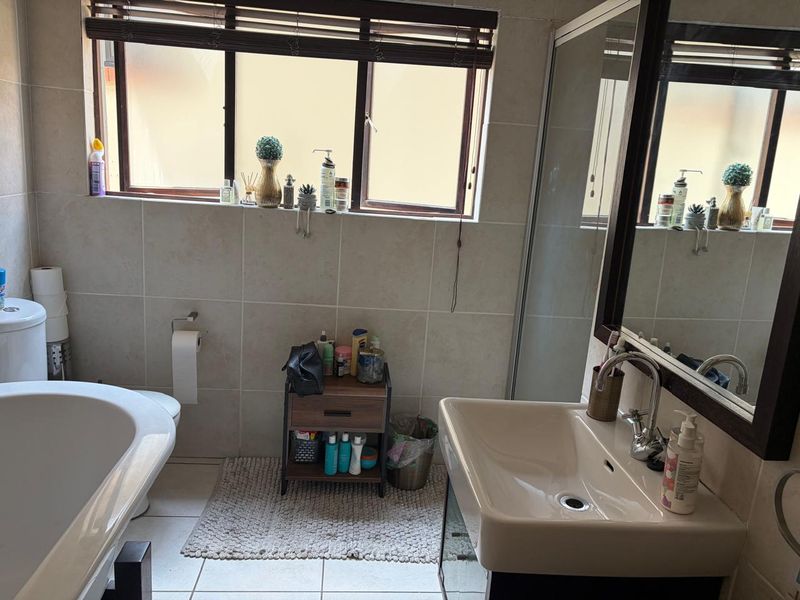 A functional bathroom featuring a freestanding bathtub, a vanity basin with a mixer tap, a shower enclosure, and neutral wall and floor tiling.
