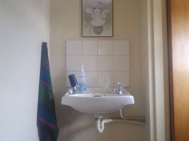A small bathroom area featuring a wall-mounted basin with a tiled splashback and exposed plumbing fixtures.