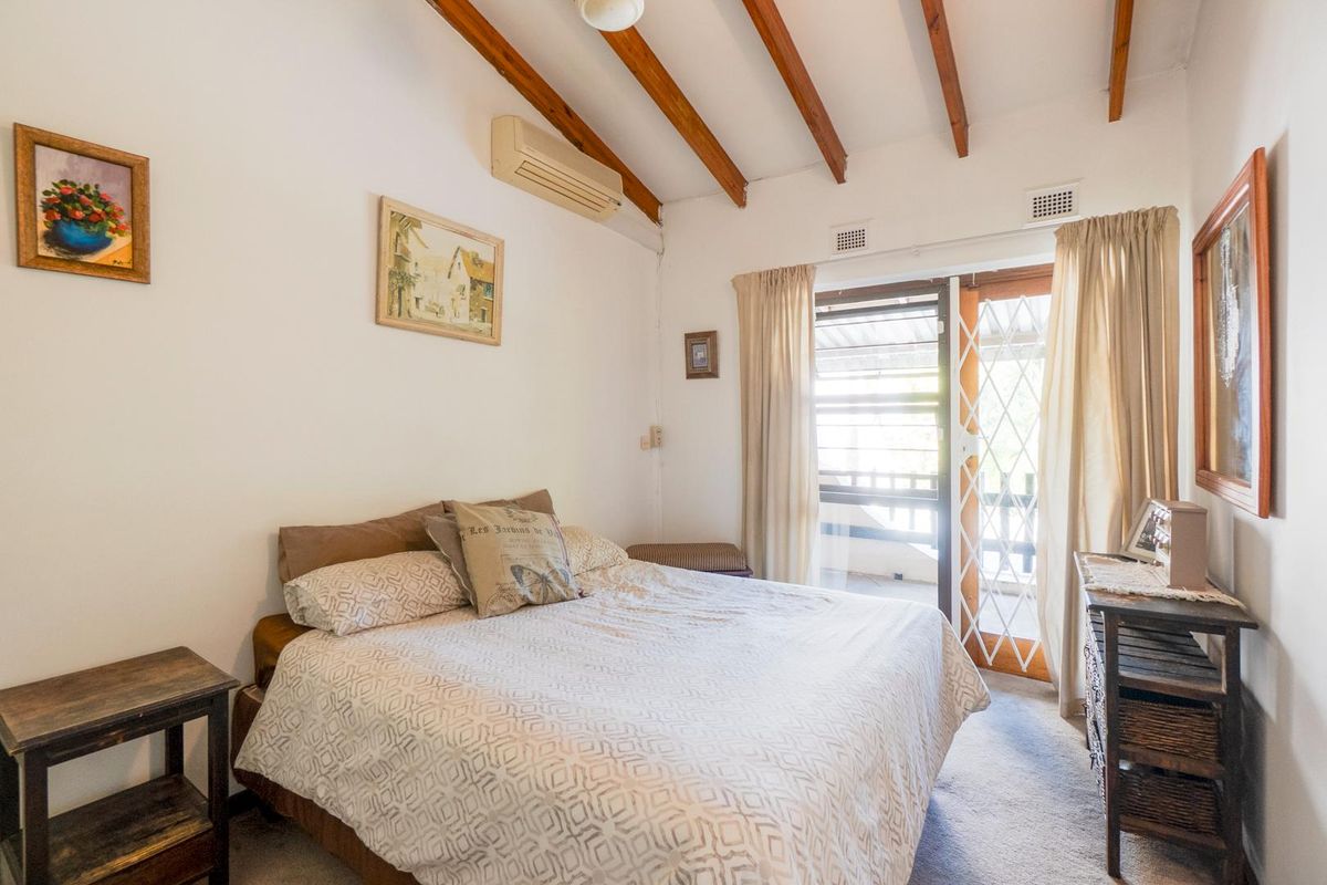 A bedroom featuring exposed timber ceiling beams, a wall-mounted air conditioning unit, and sliding glass doors providing access to an outdoor area.