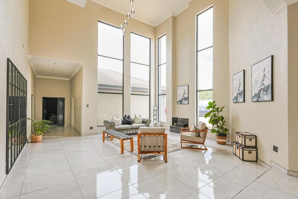 Spacious living area featuring double-volume ceilings, large floor-to-ceiling windows, polished tile flooring, and a built-in fireplace.