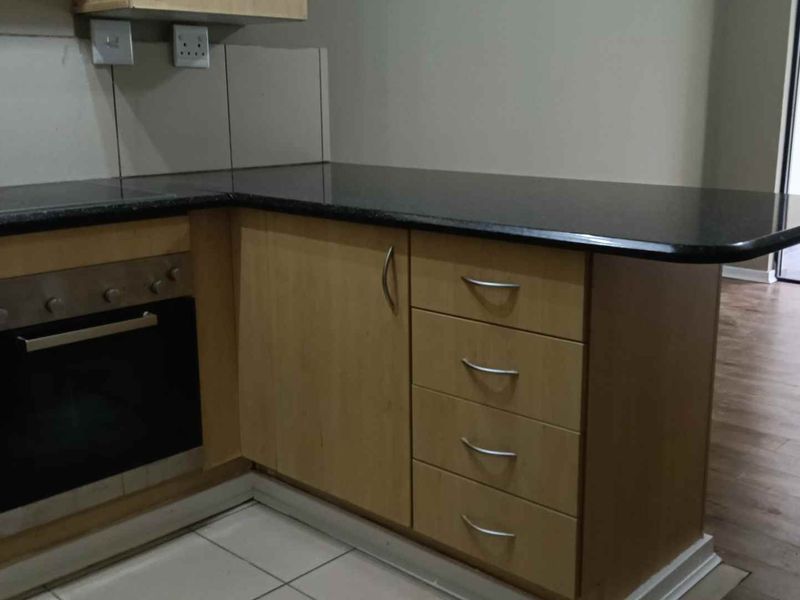 A functional kitchen area featuring light wood cabinetry, dark granite countertops, a built-in oven, and a hob, with tiled flooring and splashbacks.