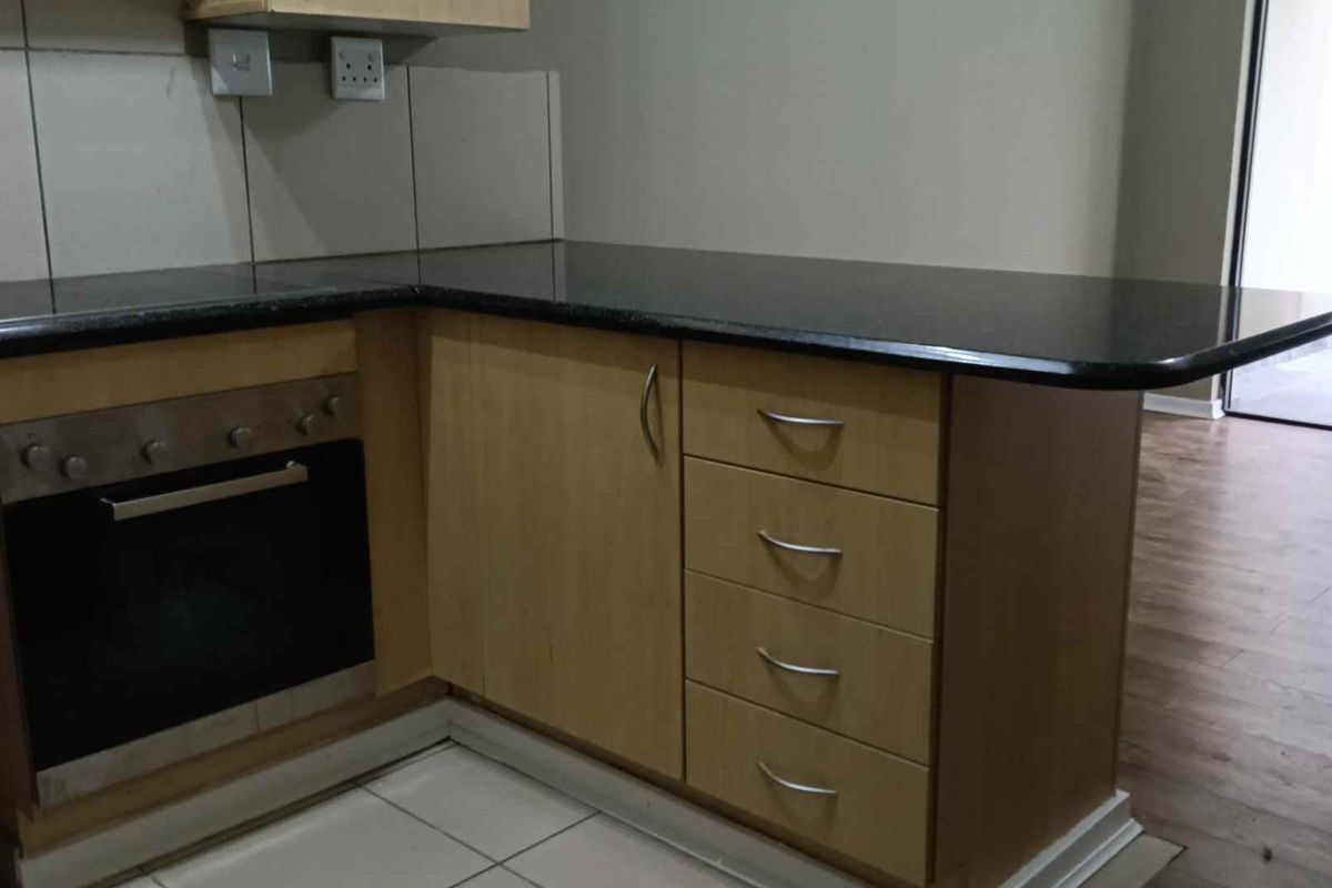 A functional kitchen area featuring light wood cabinetry, dark granite countertops, a built-in oven, and a hob, with tiled flooring and splashbacks.