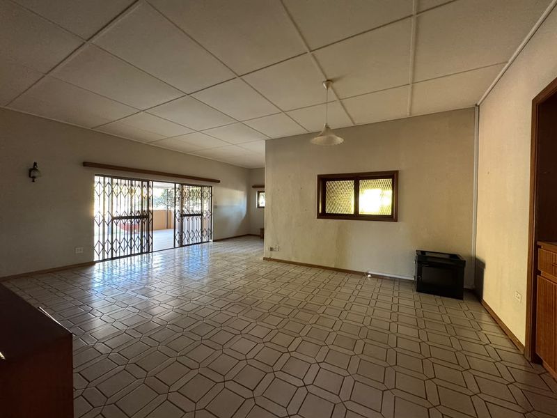 Spacious, empty living area featuring tiled flooring, a drop ceiling, and a built-in fireplace, with direct access to an outdoor patio through a security gate.