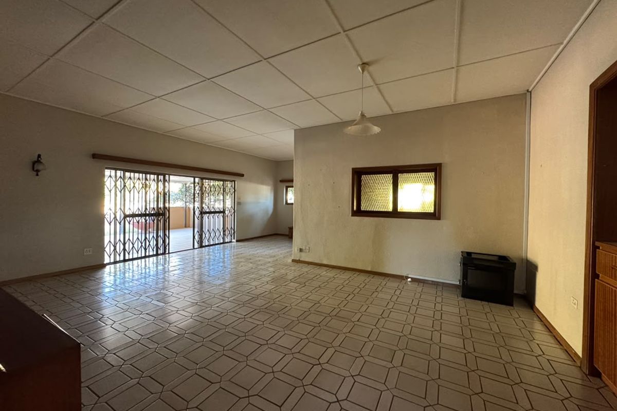 Spacious, empty living area featuring tiled flooring, a drop ceiling, and a built-in fireplace, with direct access to an outdoor patio through a security gate.