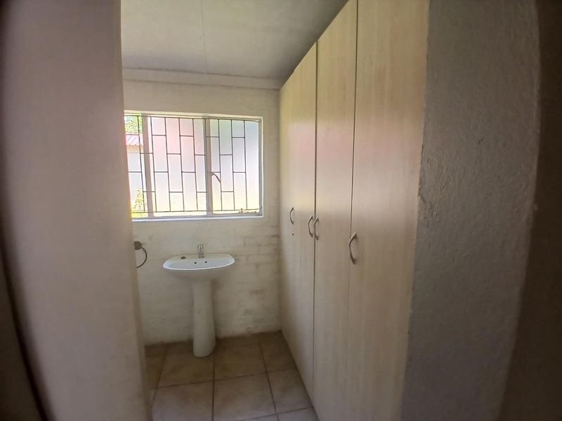 A compact bathroom featuring a pedestal basin, built-in storage cupboards, and security bars on the window.