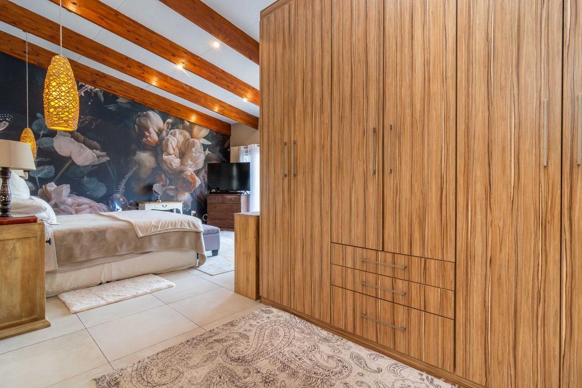 Spacious bedroom featuring exposed timber ceiling beams, large built-in wooden wardrobes, and tiled flooring with a feature floral wall.