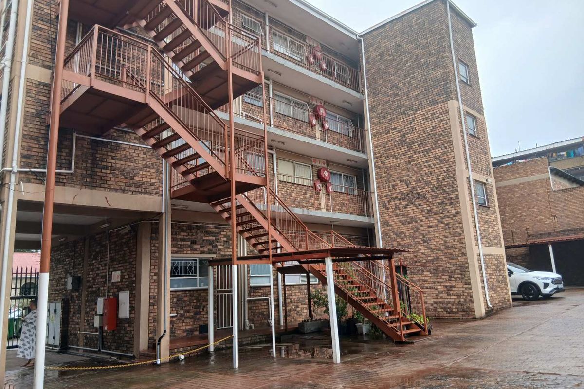 Exterior view of a multi-story apartment building featuring exposed brick facade and an external metal staircase structure.