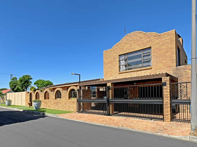 Front exterior view of a double-story face brick house featuring a secure gated entrance, paved driveway, and decorative arched brick wall detailing.