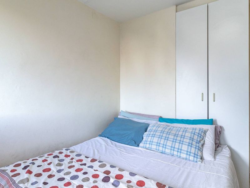A compact bedroom featuring neutral walls, tiled flooring, and a built-in white wardrobe, offering a functional space with potential for modern updates.