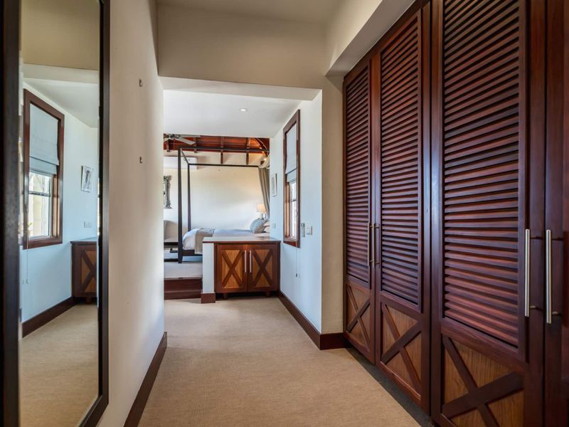 A well-maintained hallway featuring built-in wooden louvered cabinetry, leading into a spacious bedroom area with a four-poster bed.