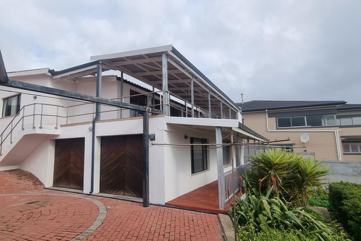 Rear exterior view of the property featuring a covered patio area, paved driveway, and multi-level structure with integrated garage doors.