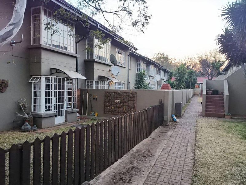 Rear view of the townhouse complex featuring brick pathways, private garden sections with picket fencing, and multi-level residential units with steel-framed windows.