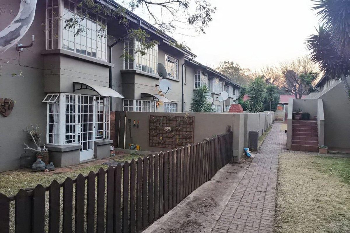 Rear view of the townhouse complex featuring brick pathways, private garden sections with picket fencing, and multi-level residential units with steel-framed windows.