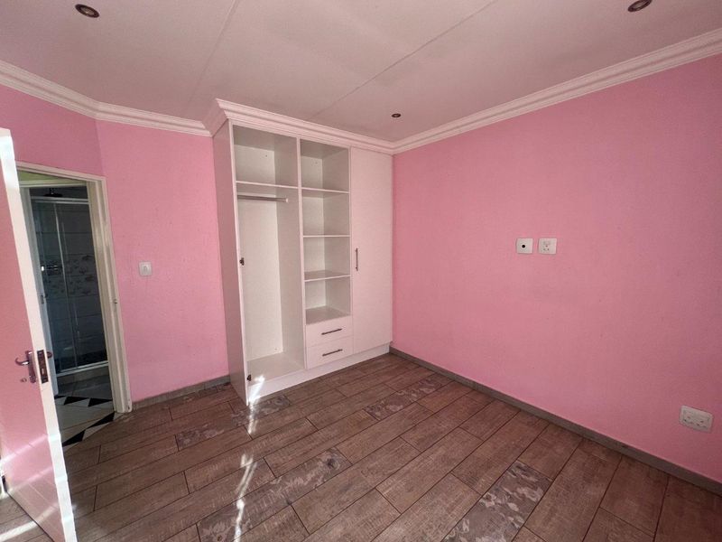 A vacant bedroom featuring wood-look tiled flooring, built-in wardrobe storage, recessed ceiling lighting, and crown molding, with an adjacent en-suite bathroom visible.