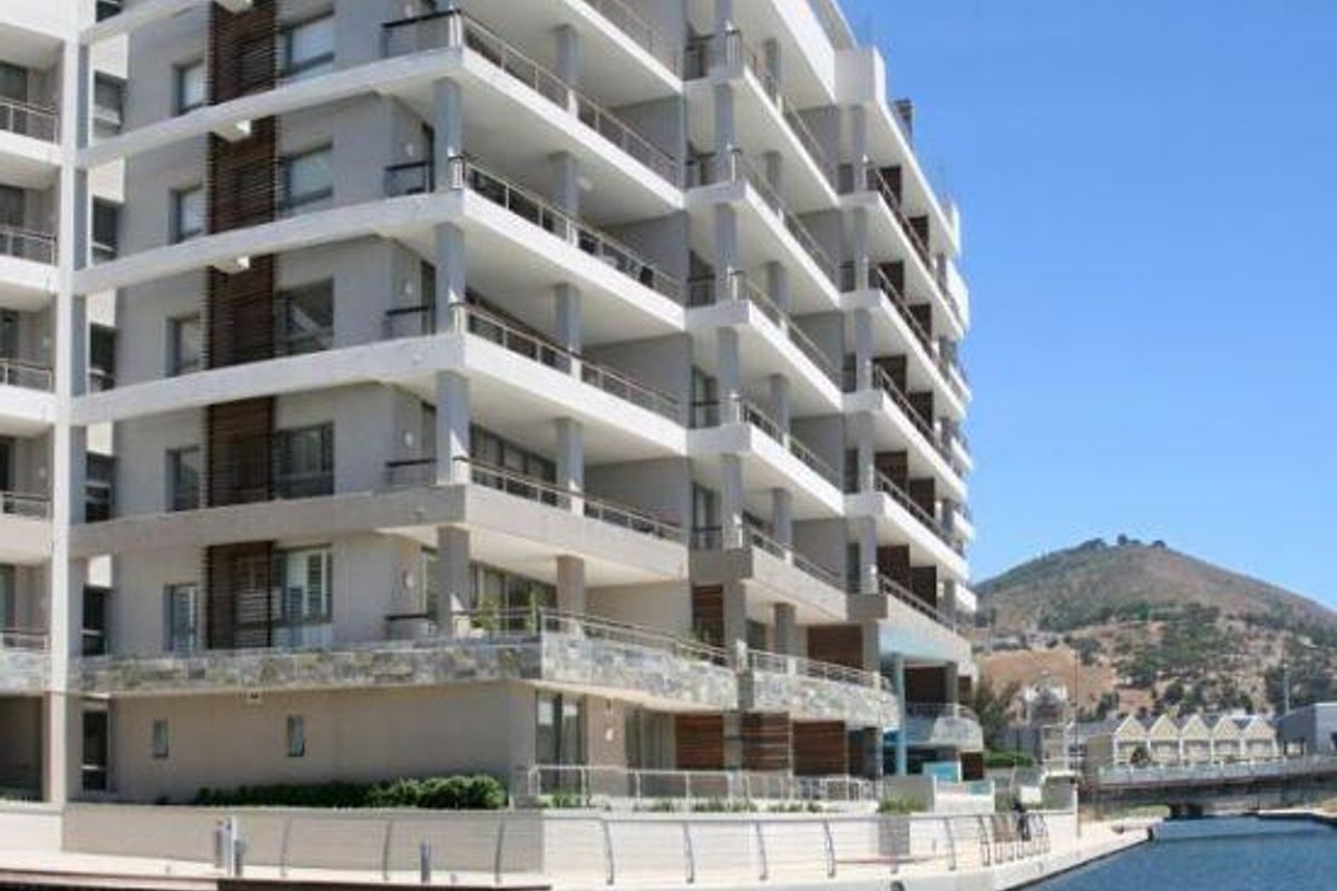 A modern multi-story apartment building featuring tiered balconies with glass balustrades, stone cladding accents, and direct waterfront access.