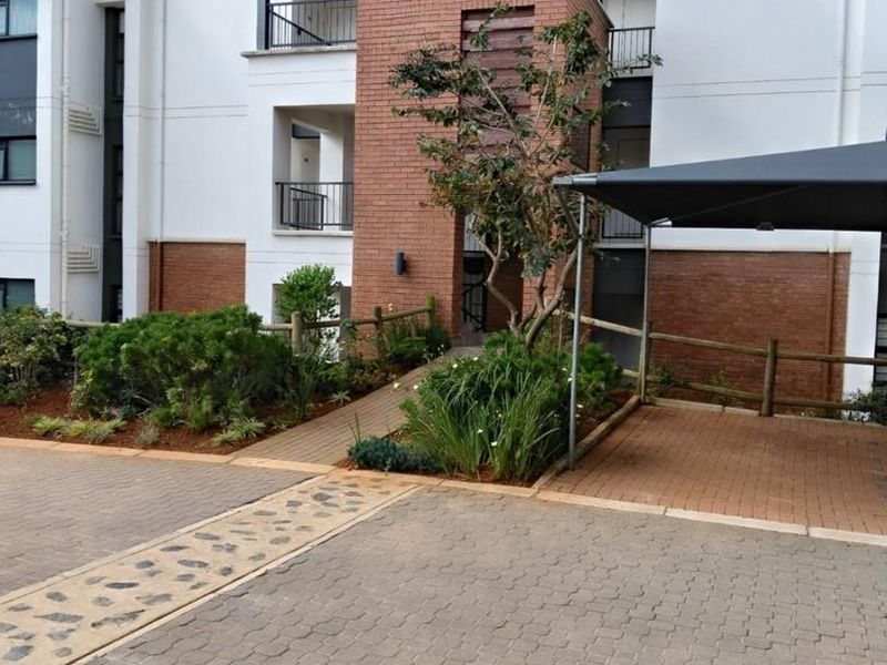 Front view of a modern apartment complex featuring brick and plaster facade, paved driveway, and covered parking area.